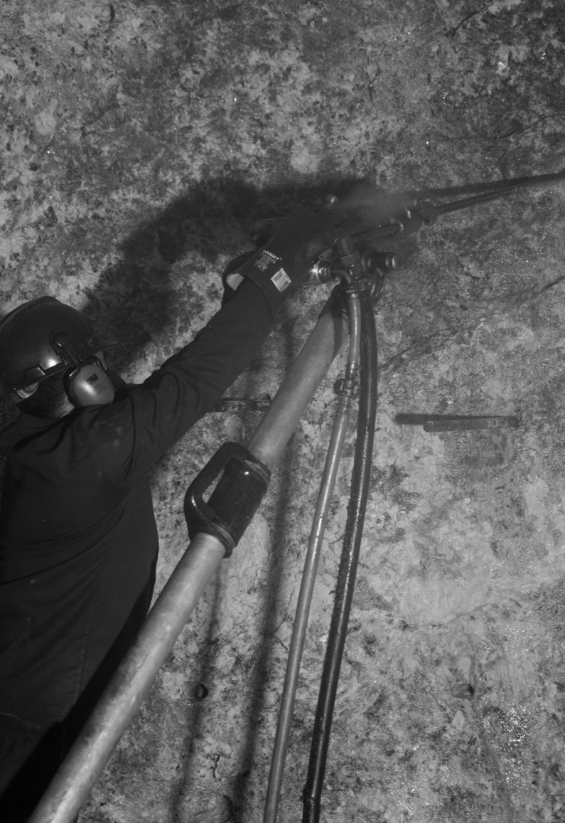 Worker drilling dynamite holes in a pegmatite wall